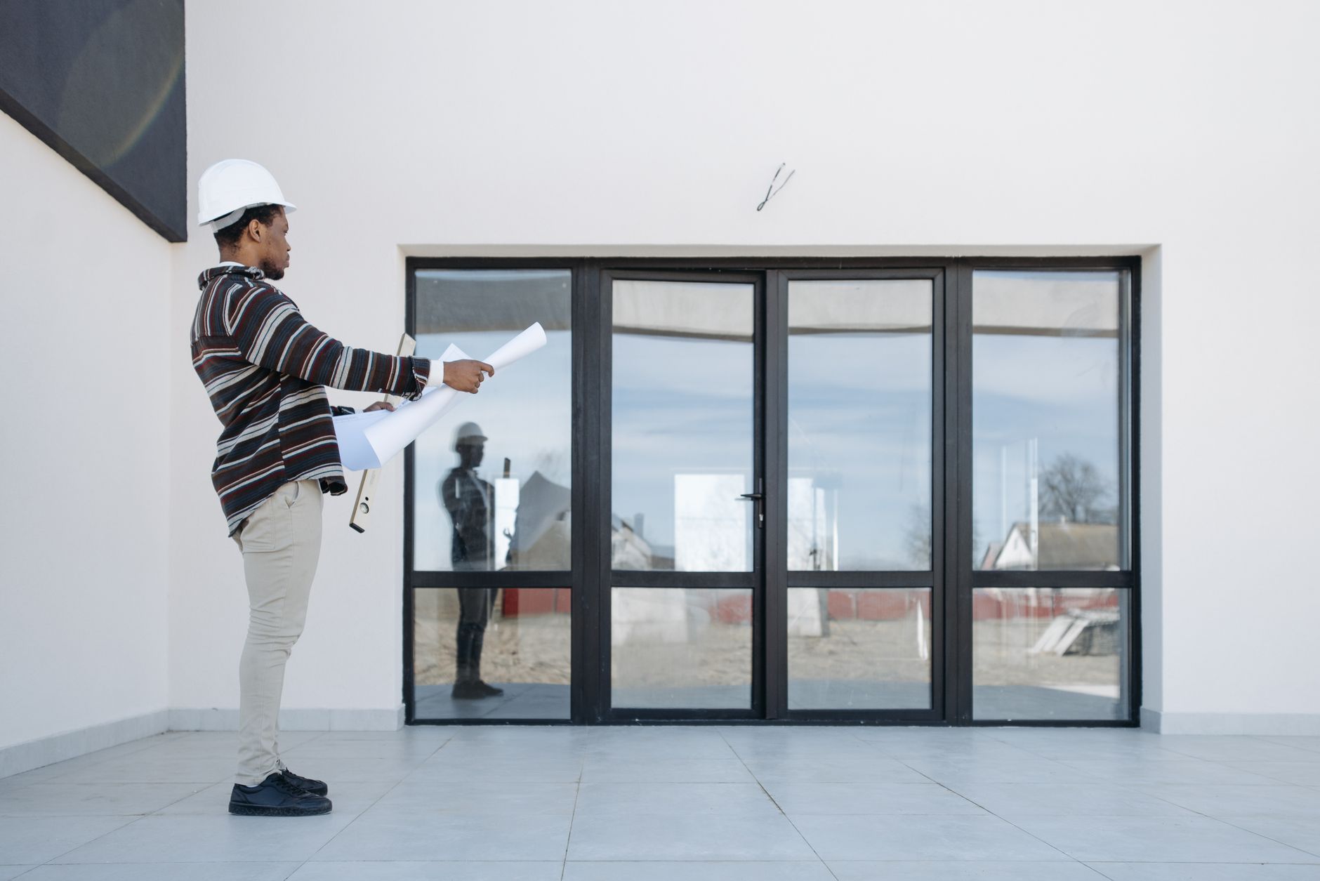 Architekt w kasku z planami przed nowoczesnym domem z przeszkleniami